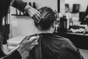 Black and white photo of hairstylist styling bride's updo at salon chair before wedding day.
