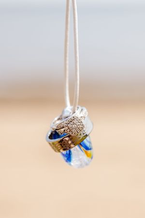 Wedding rings and blue crystal charm hanging from white ribbon in elegant detail shot.