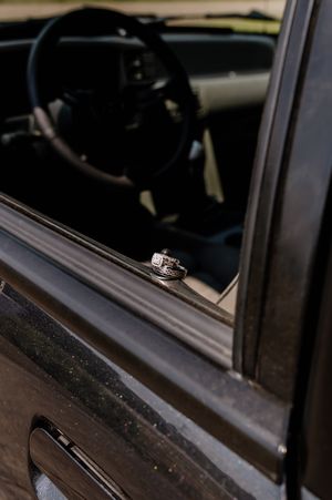 Wedding rings balanced on vintage car window ledge with steering wheel visible in background.