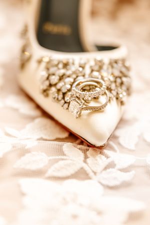 Diamond wedding rings displayed on a jeweled bridal heel on delicate lace fabric.