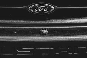 Wedding ring placed on Ford truck grille emblem in artistic black and white detail shot.