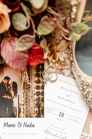 Wedding invitation for Monte and Nadia with rings, bouquet, and couple portrait flat lay.