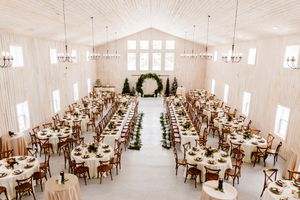 Elegant wedding reception hall with long garland-lined tables, chandeliers, and floral arch backdrop.