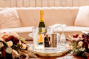 Champagne bottle in ice bucket with wedding photo card and empty flutes on a gold tray.