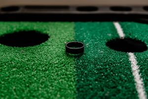 Black wedding band ring displayed on green golf putting mat with holes.