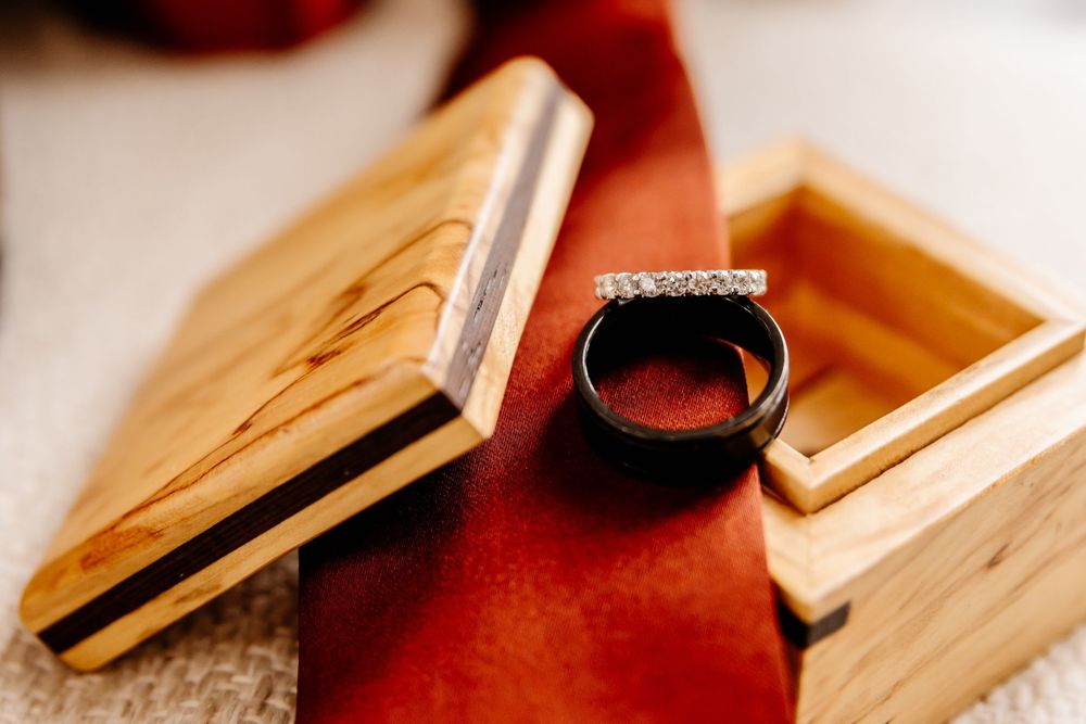 His and hers wedding bands displayed in wooden ring box on red tie.