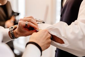 Groomsman helping adjust cufflinks on groom's white dress shirt before wedding.