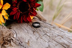 Diamond engagement ring resting on rustic wood beside vibrant red and yellow sunflowers.