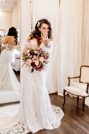 Bride in lace gown shows off her engagement ring while holding a colorful bridal bouquet.
