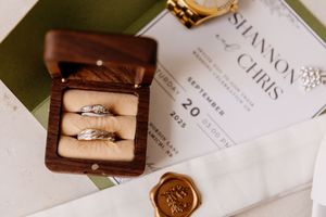 Wedding rings displayed in a wooden box beside an invitation for Shannon and Chris dated September 20.