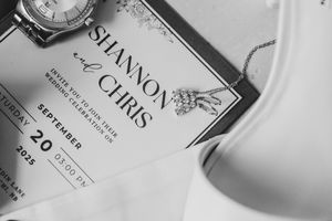 Black and white flat lay of a Shannon and Chris September 20 2025 wedding invitation with a watch and jewelry.