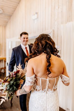 Groom smiles as bride in detailed lace off-shoulder gown holds a lush autumn wedding bouquet.