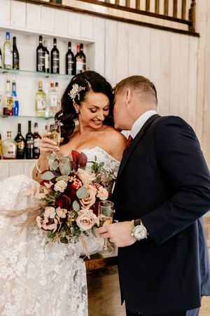 Bride and groom share a champagne toast at a rustic bar during their winter wedding reception.
