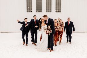 Wedding party celebrating outdoors in snow, bride and groom kissing surrounded by bridesmaids and groomsmen.