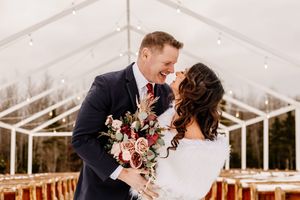Bride and groom laughing together under string lights in clear tent at romantic winter wedding ceremony.