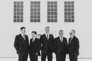 Groom and groomsmen in black suits posing outside white building, black and white.