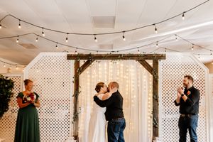 Couple shares their first kiss under a rustic wooden arch adorned with fairy lights at their wedding.