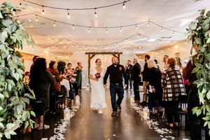 Newlyweds walk down the aisle as guests celebrate with flower petals in a warmly lit venue.