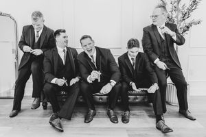 Groomsmen laughing and posing on bench in black suits, black and white photo.