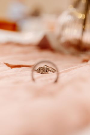 Close-up of elegant diamond engagement ring and wedding band on soft pink fabric with bokeh background.