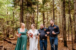 Bride groom and wedding party laugh together while walking through a sunlit forest on the wedding day.