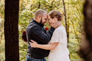 Bride and groom share an intimate forehead-to-forehead moment surrounded by lush green trees outdoors.