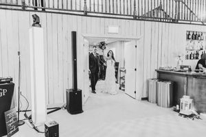 Bride and groom make grand entrance through doorway into rustic barn reception venue in black and white photo.