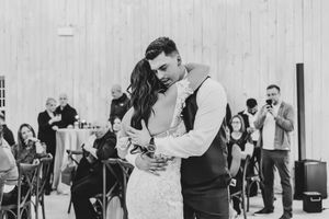 Bride and groom embrace during emotional first dance in black and white wedding reception photo.
