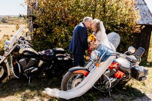 Bride and groom share a romantic kiss beside vintage motorcycles during their outdoor fall wedding celebration.