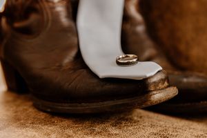 Gold wedding band resting on a white tie draped over rustic brown leather cowboy boots.