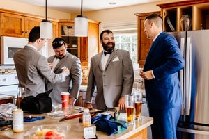 Groomsmen in suits gather around a kitchen island, laughing and preparing for a wedding celebration.