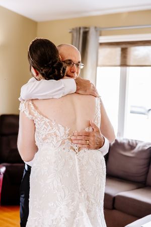 Emotional father-daughter embrace as bride in lace backless gown hugs him before wedding ceremony.