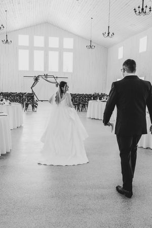 Black and white photo of bride and groom entering elegant white barn wedding reception hall.