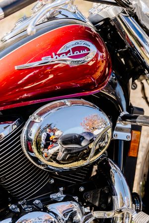 Close-up of a red Honda Shadow motorcycle tank with chrome engine cover reflecting autumn scenery.