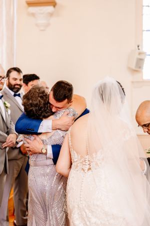 Groom in blue suit shares emotional hug with mother at the wedding altar ceremony.