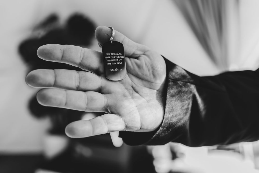 Black and white close-up of hand holding dog tag with engraved text message.