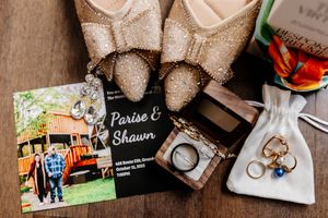 Wedding flat lay with glittery cowboy boots, invitation for Parise and Shawn, rings, and accessories on wooden surface.