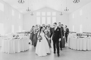 Black and white photo of bride and groom leading wedding party into elegant reception hall with draped walls.