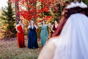 Bridesmaids in colorful gowns react with joy as bride approaches during outdoor fall wedding ceremony.