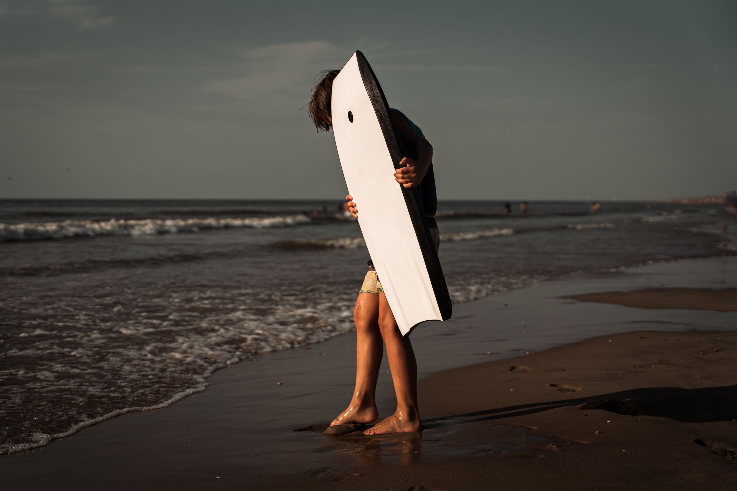 Legs walking along a moody beach shoreline at dusk.
