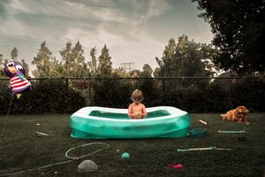 Green kiddie pool in backyard with toys under cloudy sky.