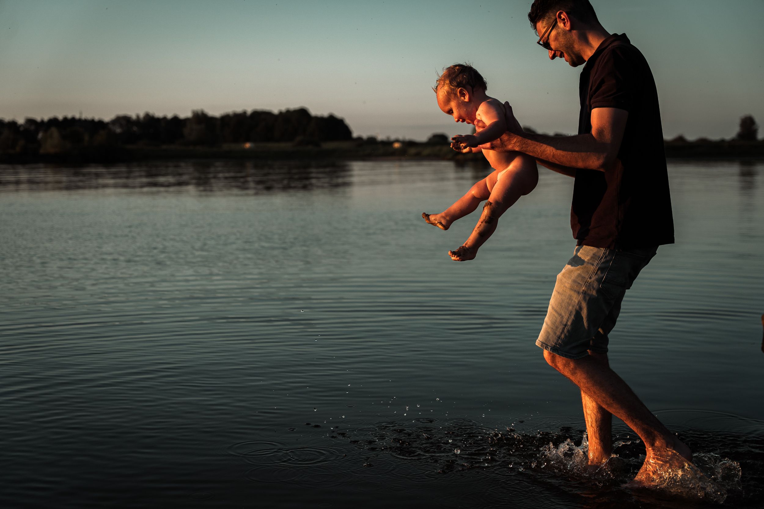 Silhouettes playing and splashing in lake water during sunset.