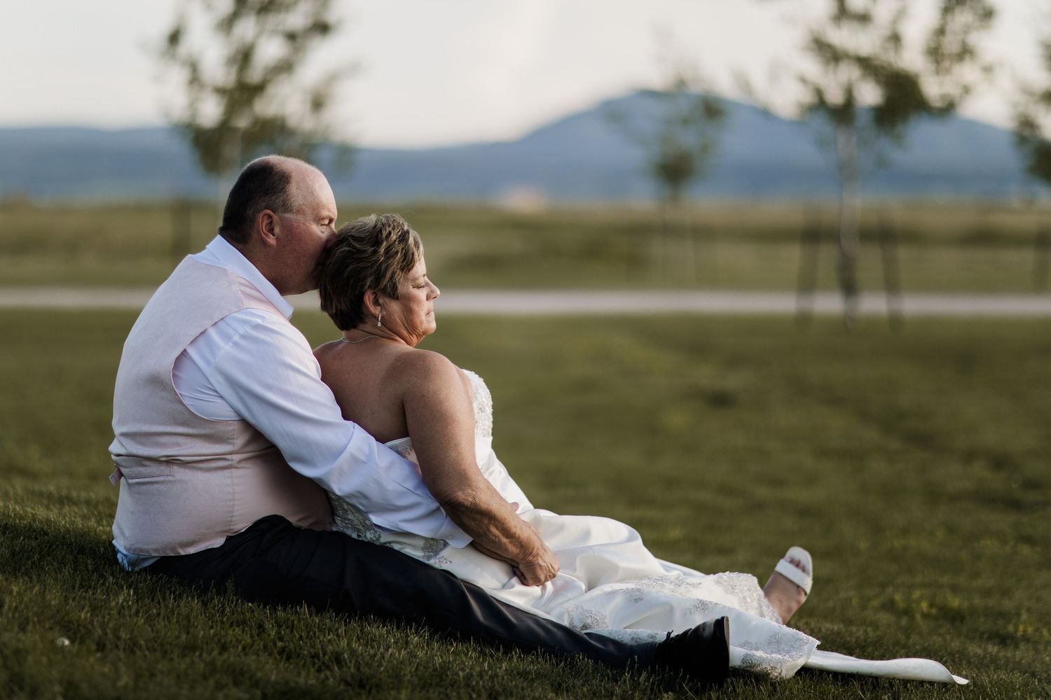 Couple relaxing together on grassy hill with mountain landscape in background.