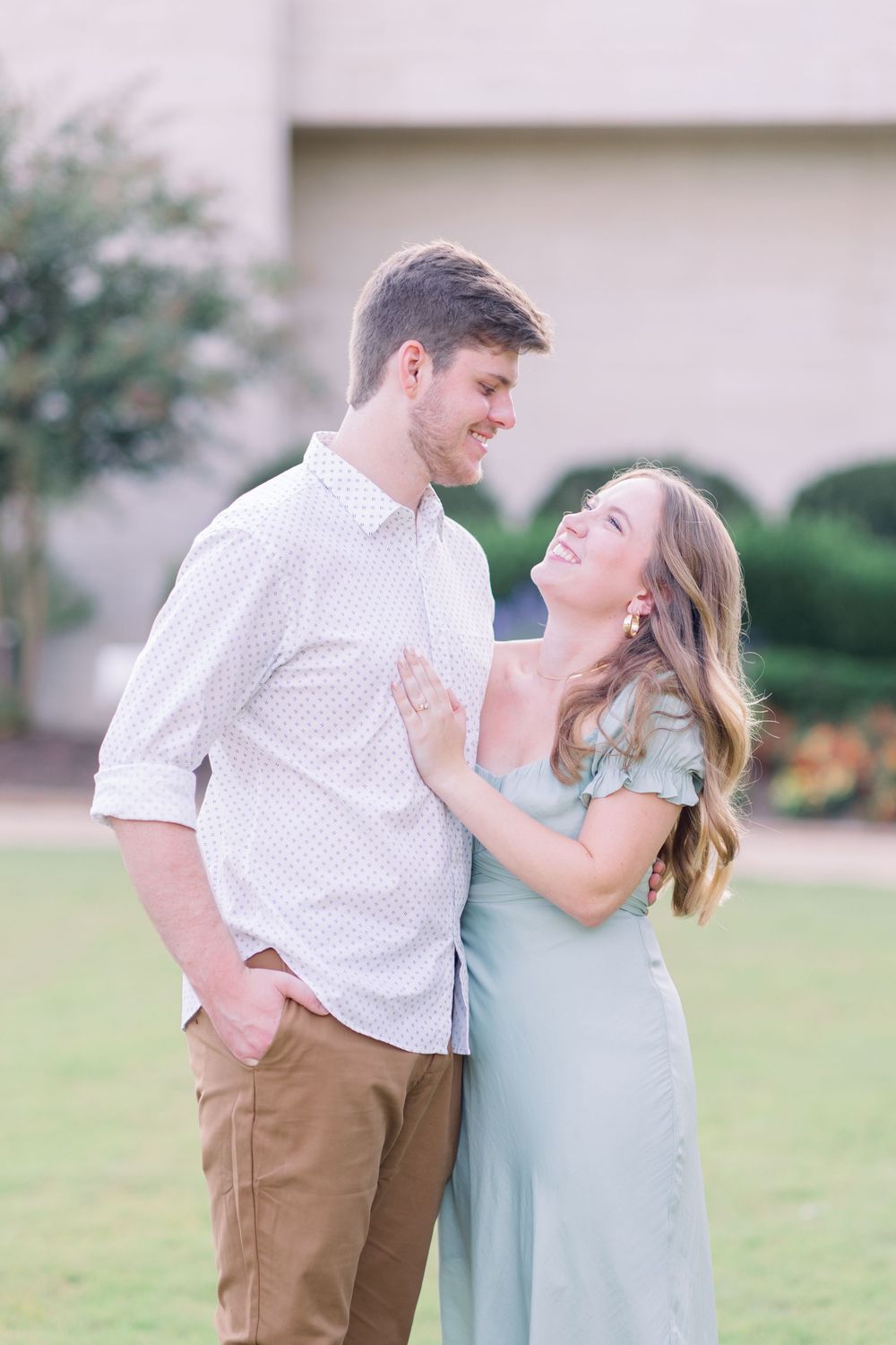 A romantic couple shares a tender moment outdoors, with her in a light blue dress and him in a white patterned shirt.