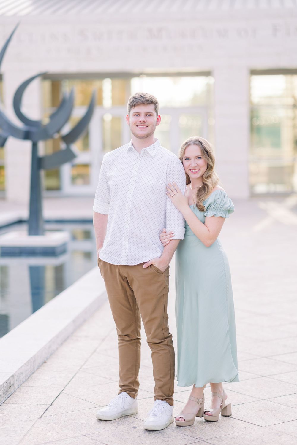 A couple poses together outdoors wearing coordinated white and mint green outfits for engagement photos.