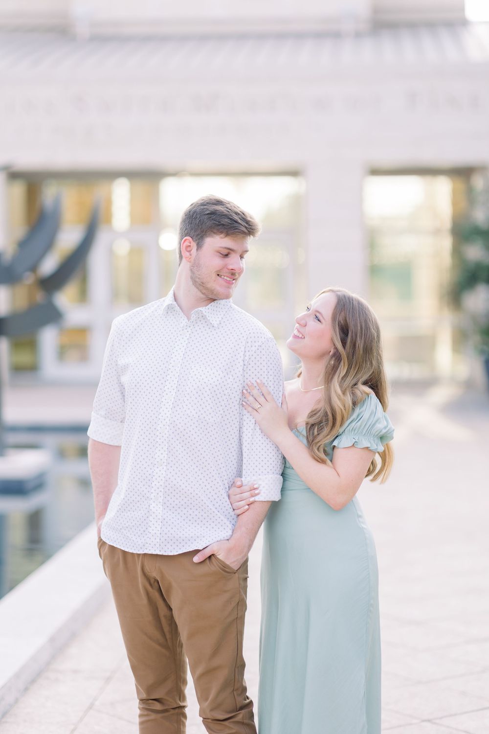 A couple shares a romantic moment outdoors, with her wearing a mint green dress and him in a white shirt and khaki pants.