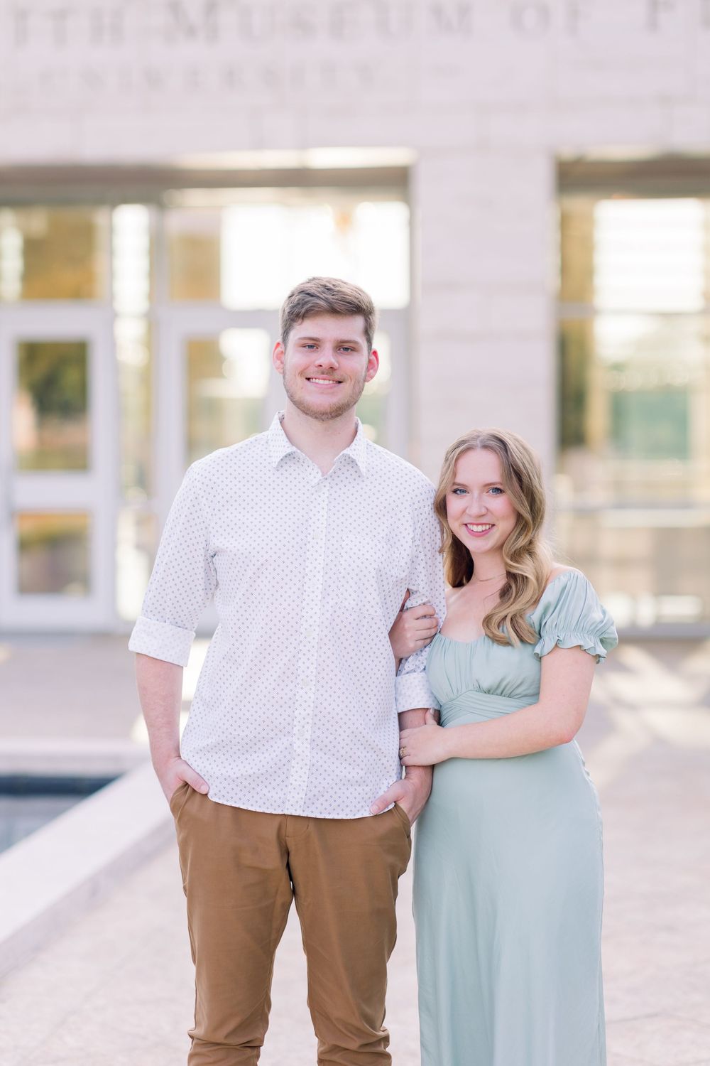 A couple poses together outdoors in coordinated outfits of white and mint green against a light neutral background.