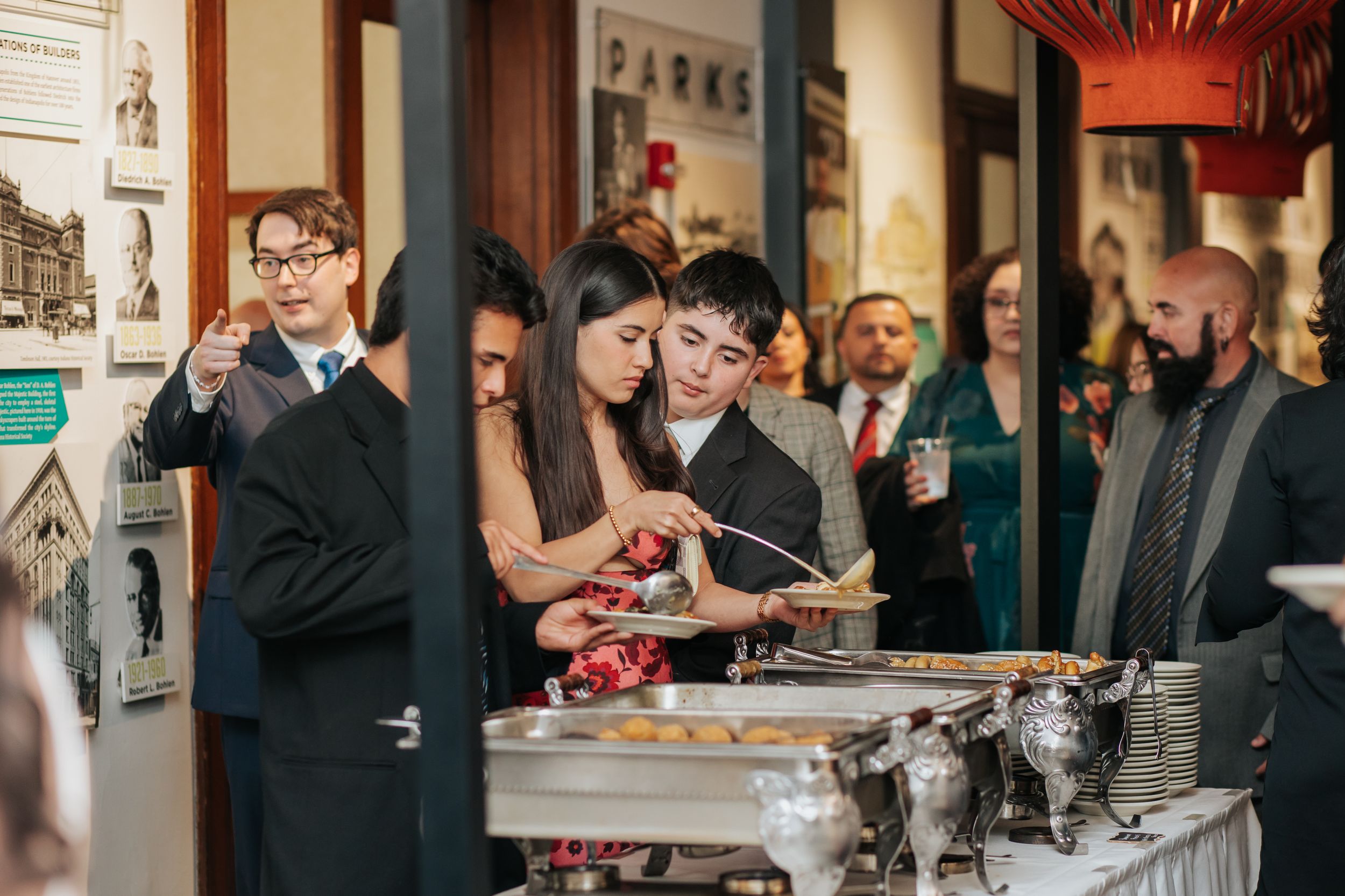 A group of people enjoying drinks and socializing at a crowded bar or event space with framed artwork on the walls.