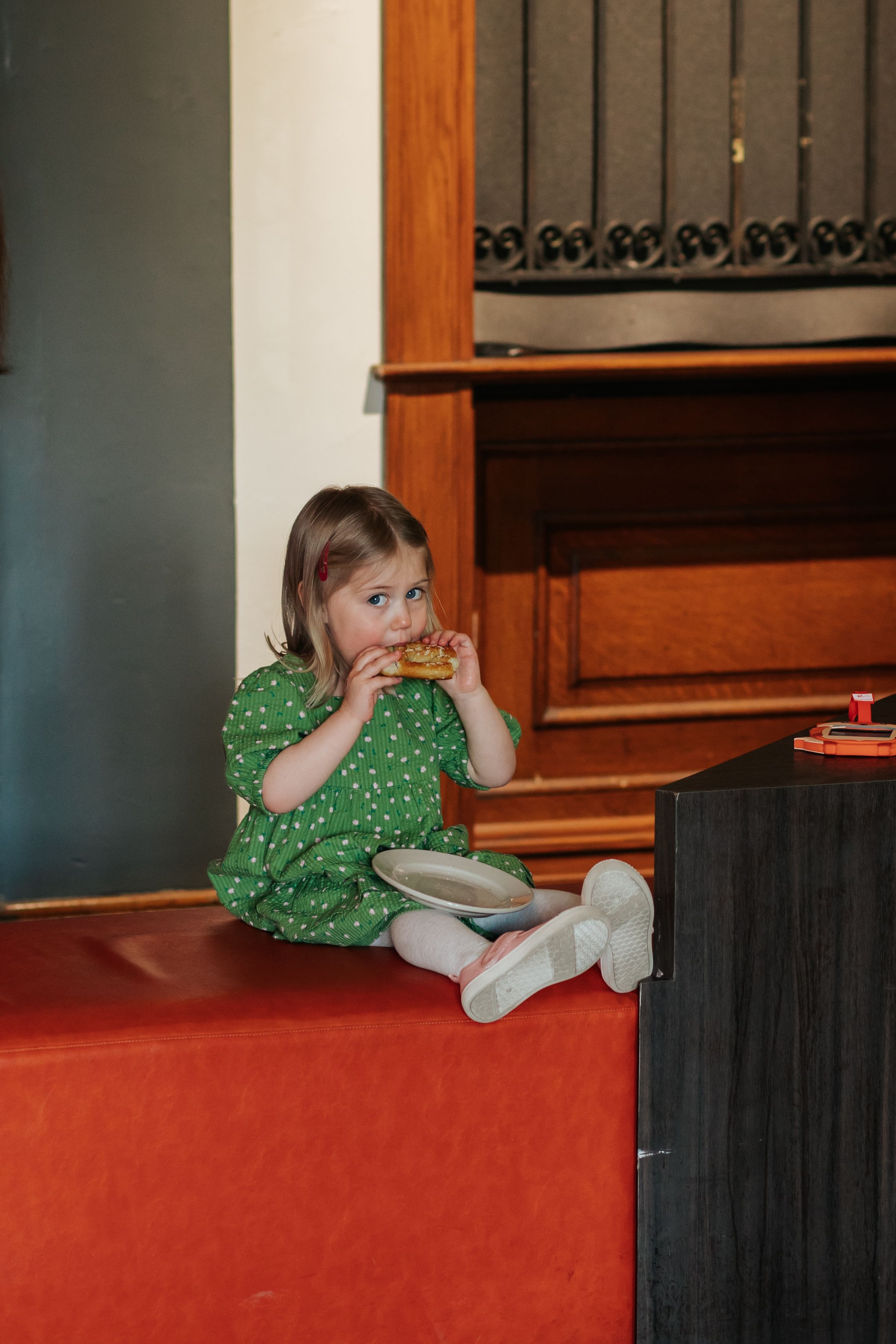A small child in a green dress lies on a red carpeted floor near wooden cabinets.