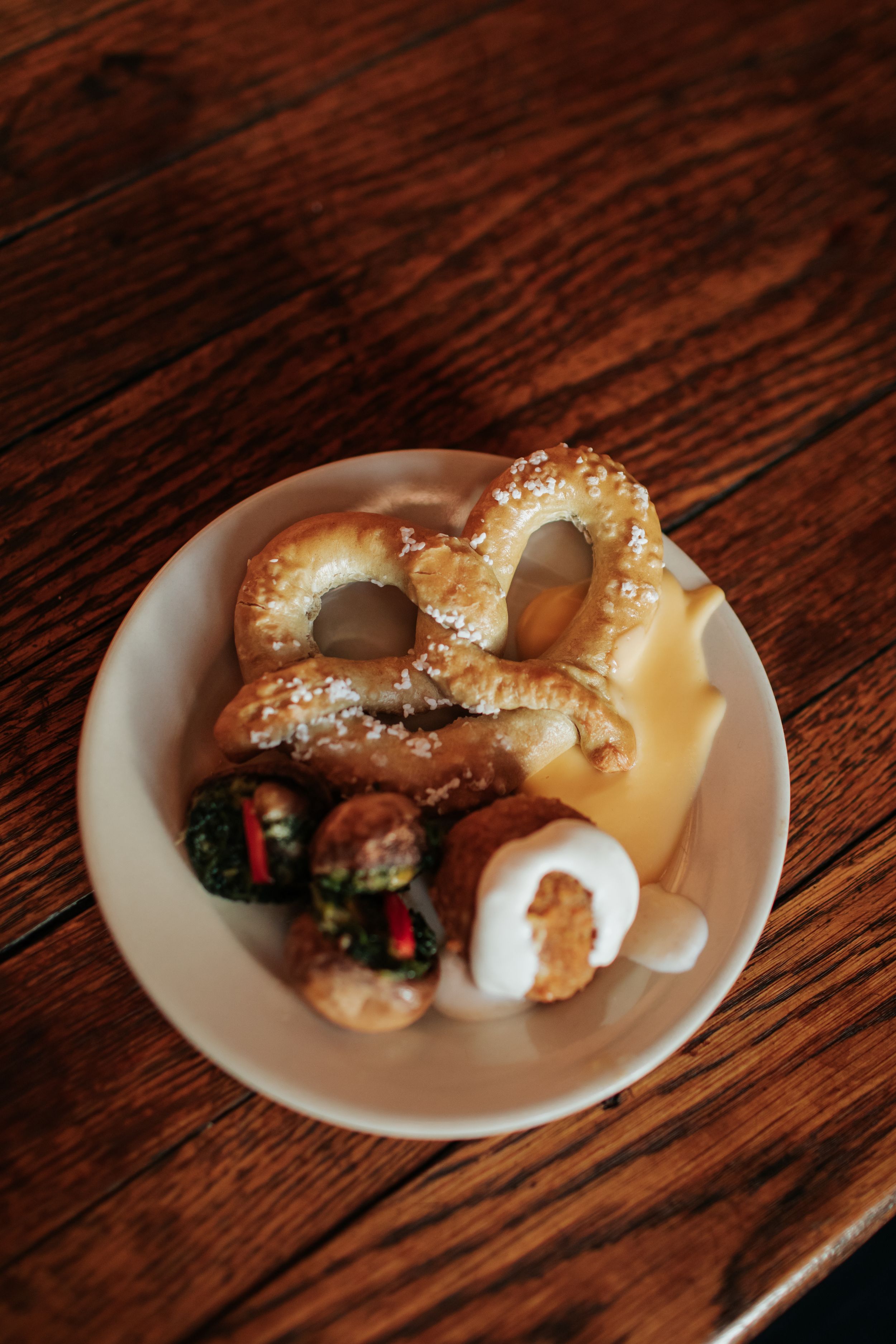Freshly baked pretzel bites with melted cheese sauce and garnish arranged on a white plate atop a wooden table.
